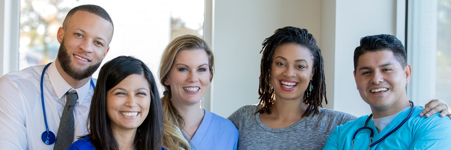 Diverse group of nurses, doctors, and other healthcare professionals are standing together confidently in a hospital hallway.